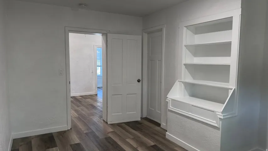 Wood-finish flooring, white painted walls, built-in shelving, white trim, and white paneled doors