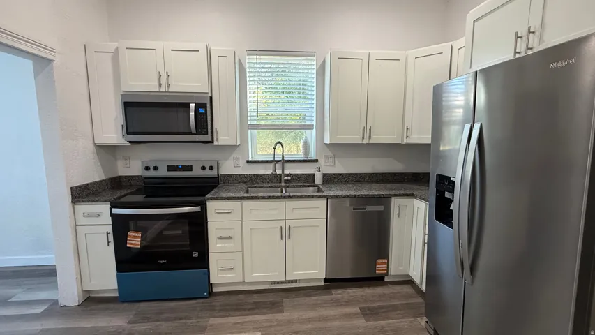 Kitchen featuring white shaker cabinetry, stainless steel appliances, dark speckled countertops, and wood-finish flooring