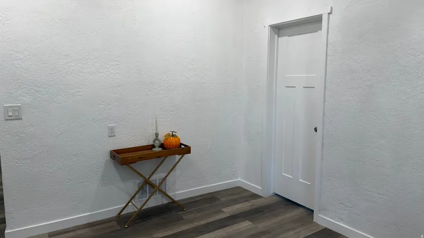 Clean white walls with textured finish, wood-finish flooring, white trim, and a white interior door with a three-panel design