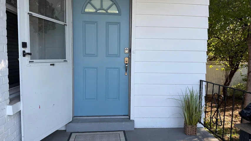 Blue paneled entry door with an arched transom window, white horizontal siding, and a black wrought iron railing