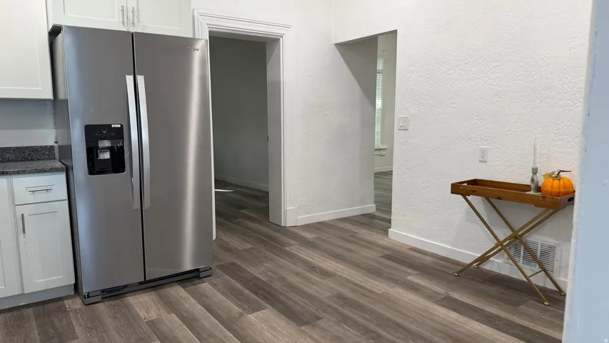 Stainless steel side-by-side refrigerator, white flat-panel cabinetry, dark speckled countertop, wood-finish flooring, and white textured walls