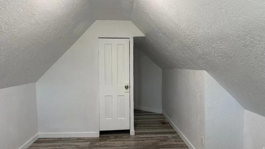 Sloped ceilings, wood-finish flooring, white paneled door, and white painted walls