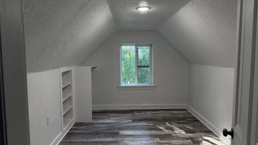 Wood-finish flooring, built-in shelving, white trim, recessed lighting, and a single window