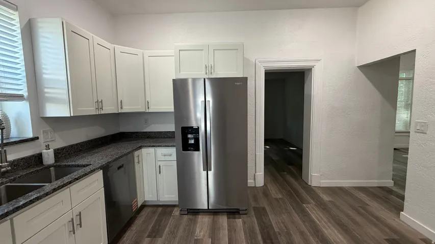 Kitchen featuring stainless steel appliances, white cabinetry, dark speckled countertops, a double basin sink, and wood-finish flooring