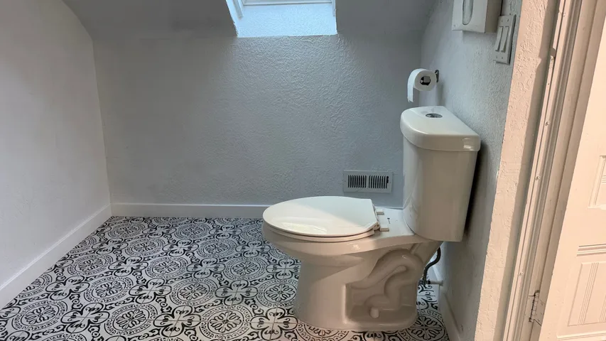 White toilet with a patterned floor, white wall texture, and a skylight