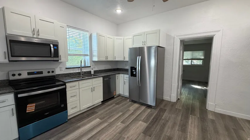 Kitchen featuring white shaker cabinetry, stainless steel appliances, granite countertops, and wood-finish flooring