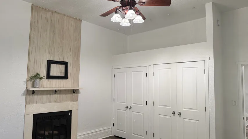 Wood-finish accent wall with mantel, gas fireplace, and integrated ceiling fan