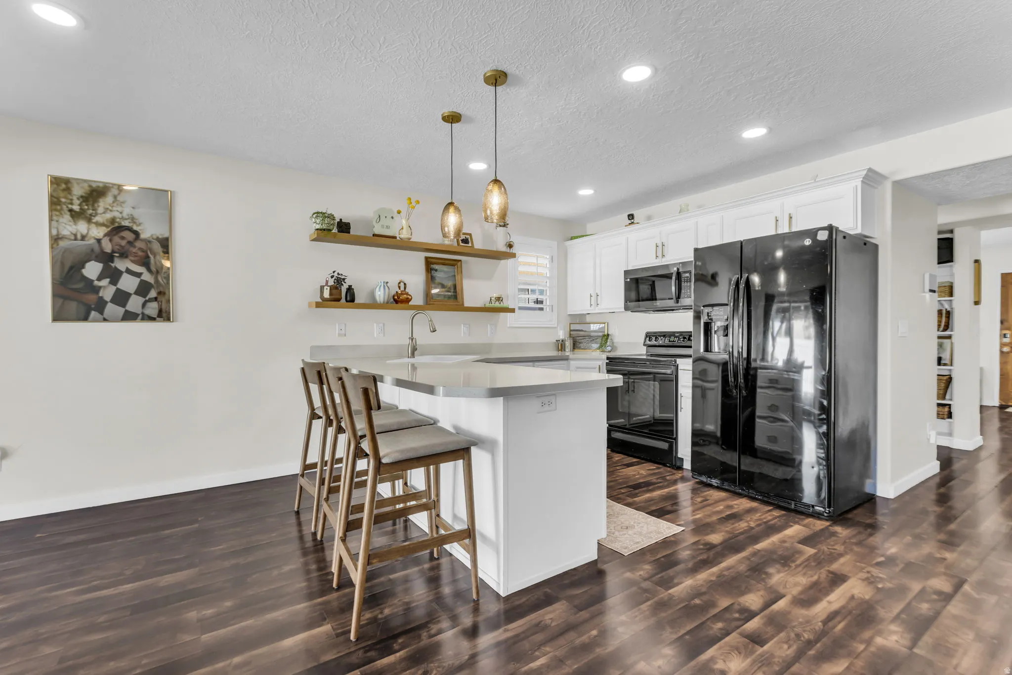 White cabinets, floating shelves, pendant lighting, and black appliances. All appliances included! Sellers willing to include floor allowance