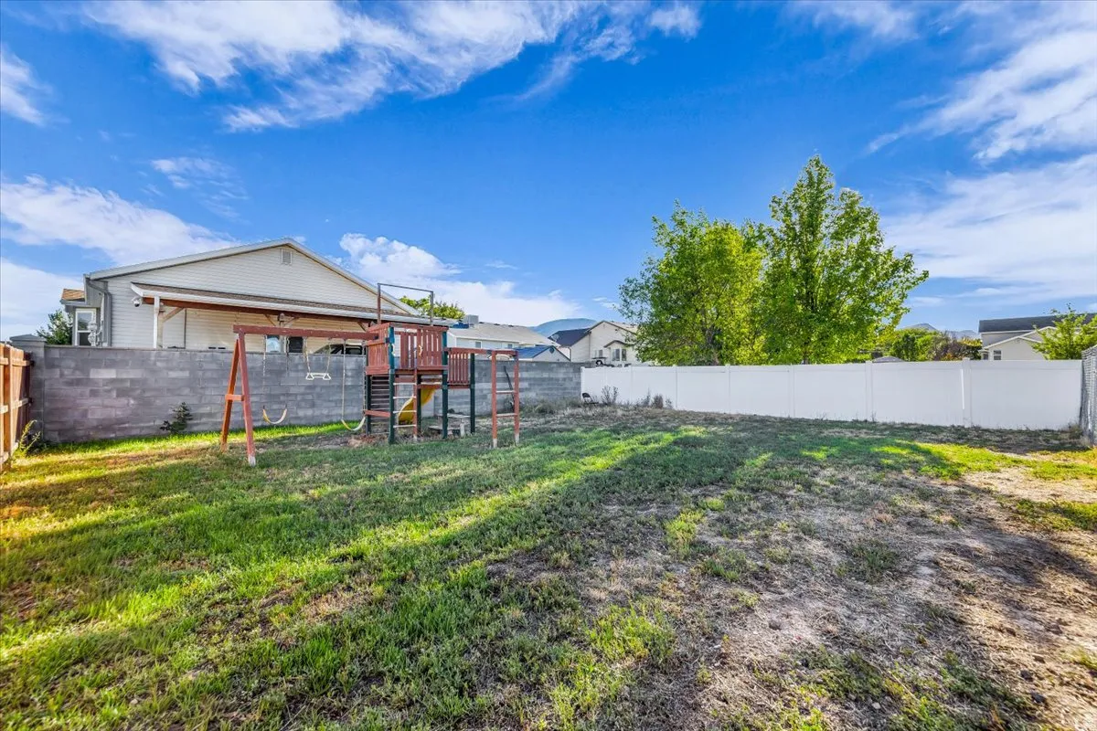 Expansive backyard with a covered patio, concrete block wall, and white vinyl fencing