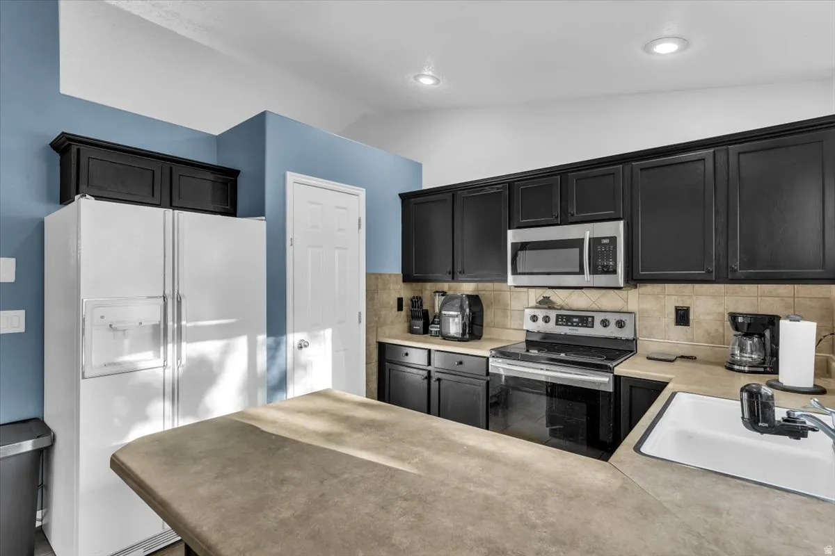 Kitchen featuring black cabinetry, stainless steel appliances, neutral-toned countertops, and a tiled backsplash