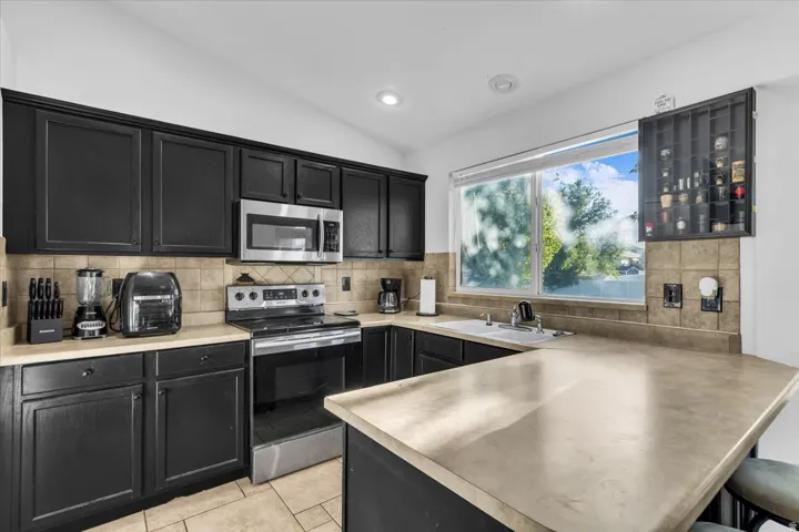 Kitchen featuring dark cabinetry, stainless steel appliances, tile backsplash, and light-toned countertops