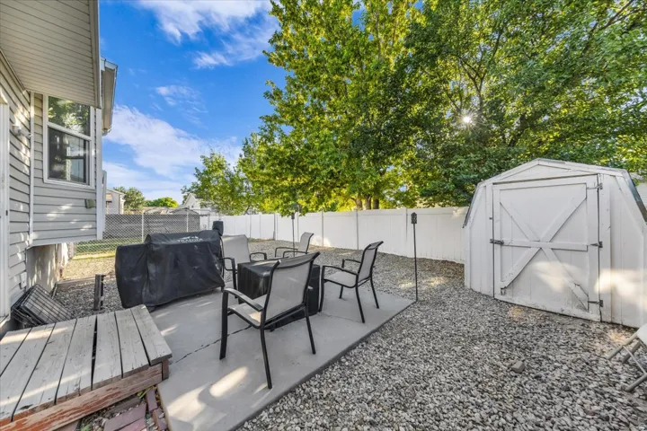 Outdoor patio with concrete slab and gravel landscaping, featuring a white storage shed and privacy fencing