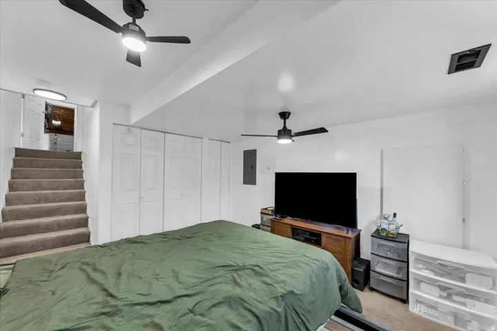 Carpeted stairs leading to an open doorway, multiple bifold closet doors, and two ceiling fans with integrated lighting