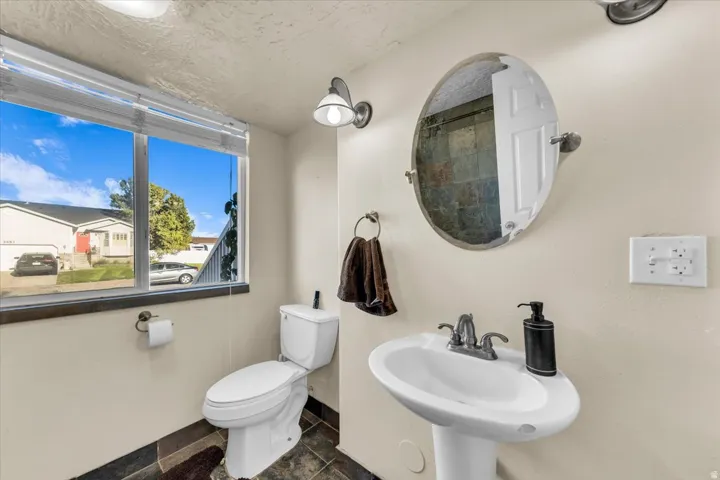 Pedestal sink with chrome fixtures, oval wall mirror, and natural stone tile flooring