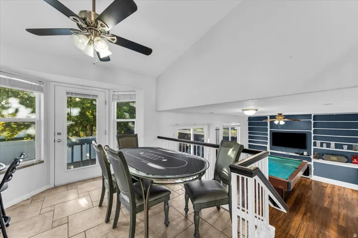 Vaulted ceiling with ceiling fan, tile flooring, and multiple windows, overlooking a lower level featuring wood-finish flooring and a built-in entertainment wall