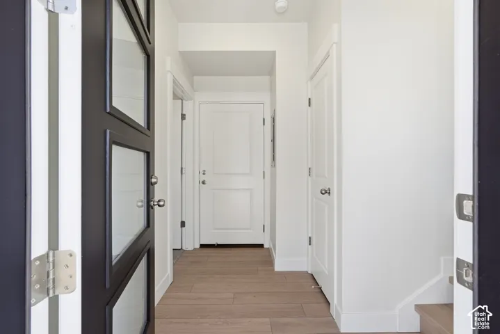 Bright hallway with wood-finish flooring, white painted walls, and multiple white six-panel doors