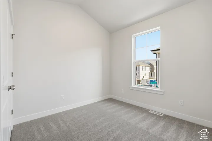 Vaulted ceiling, neutral wall tones, gray carpet, white trim, and a white-framed window