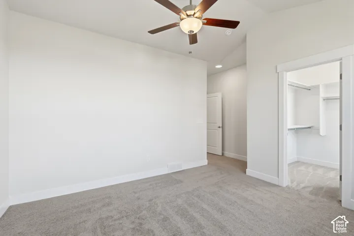 Neutral-toned carpeting throughout, ceiling fan with integrated lighting, and a walk-in closet with built-in shelving and hanging rods