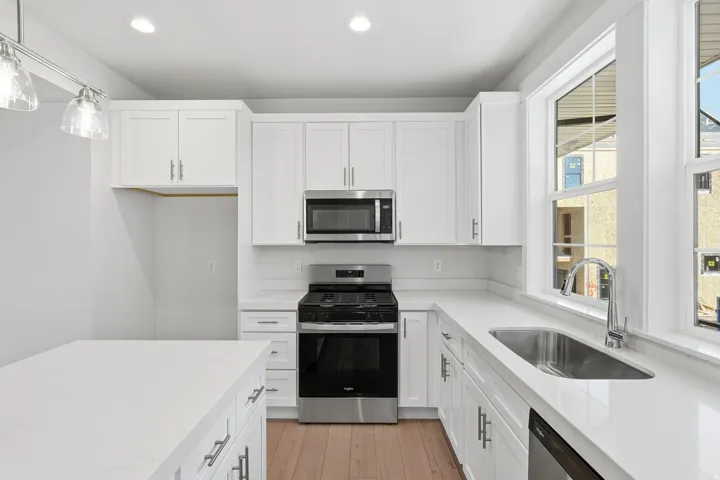 White cabinetry with stainless steel hardware, stainless steel appliances, light-toned wood-finish flooring, and a large window above the sink