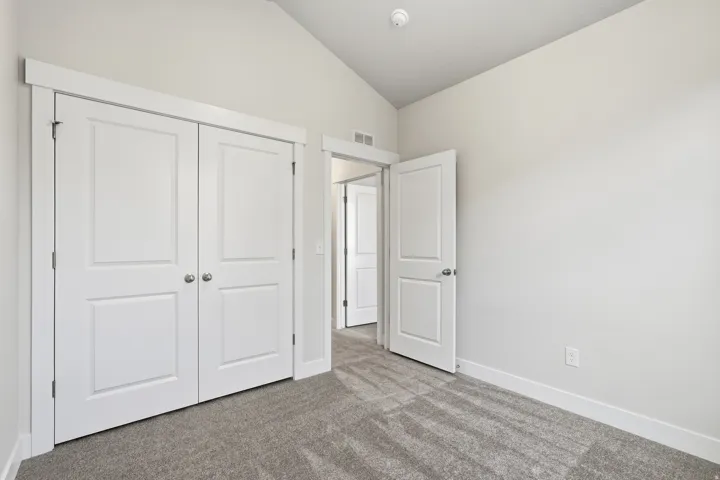 Bright bedroom featuring dual white panel closets with polished hardware, neutral wall finishes, and plush carpeting throughout