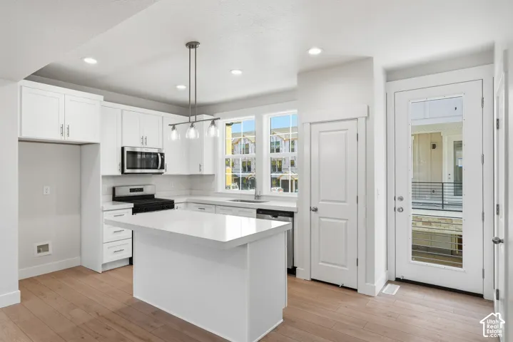 Modern kitchen featuring white shaker cabinetry, stainless steel appliances, a center island with a solid surface countertop, wood-finish flooring, and recessed lighting