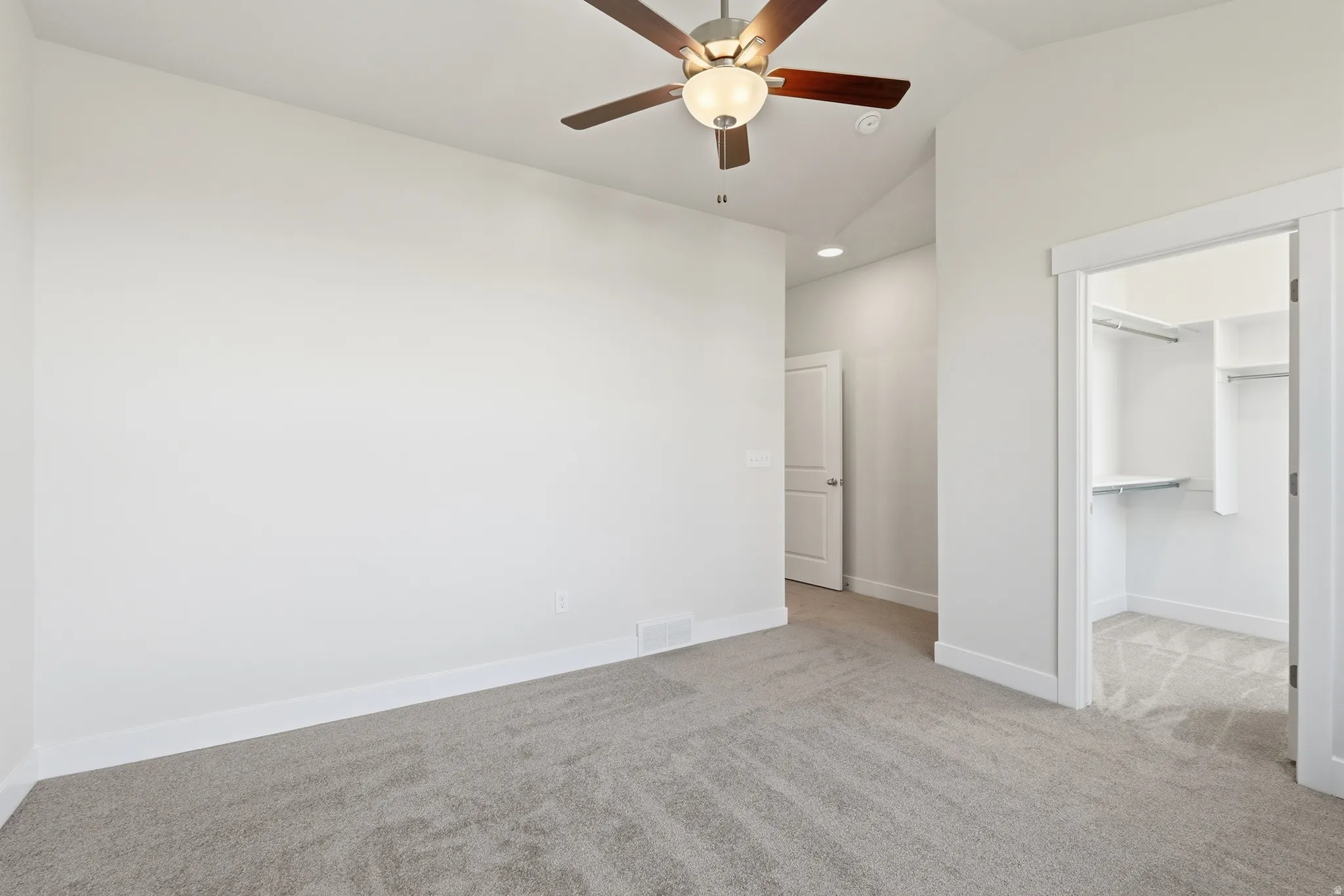 Wall-to-wall carpeting throughout, a ceiling fan with integrated lighting, and an open closet with shelving and hanging rods