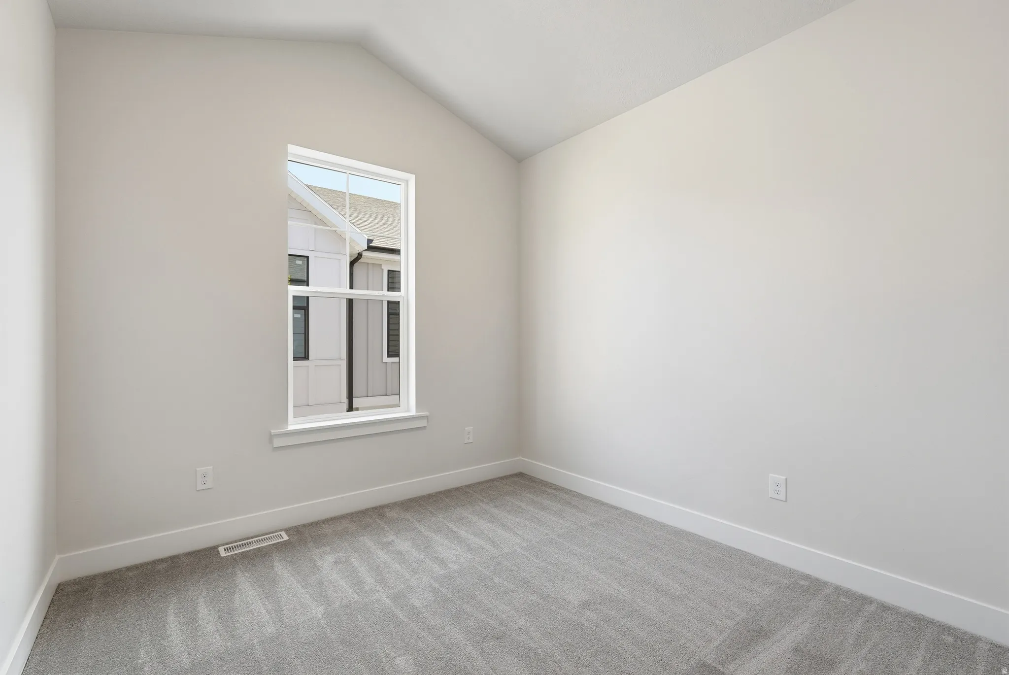 Vaulted ceiling with a single window, light-colored walls, and gray carpet