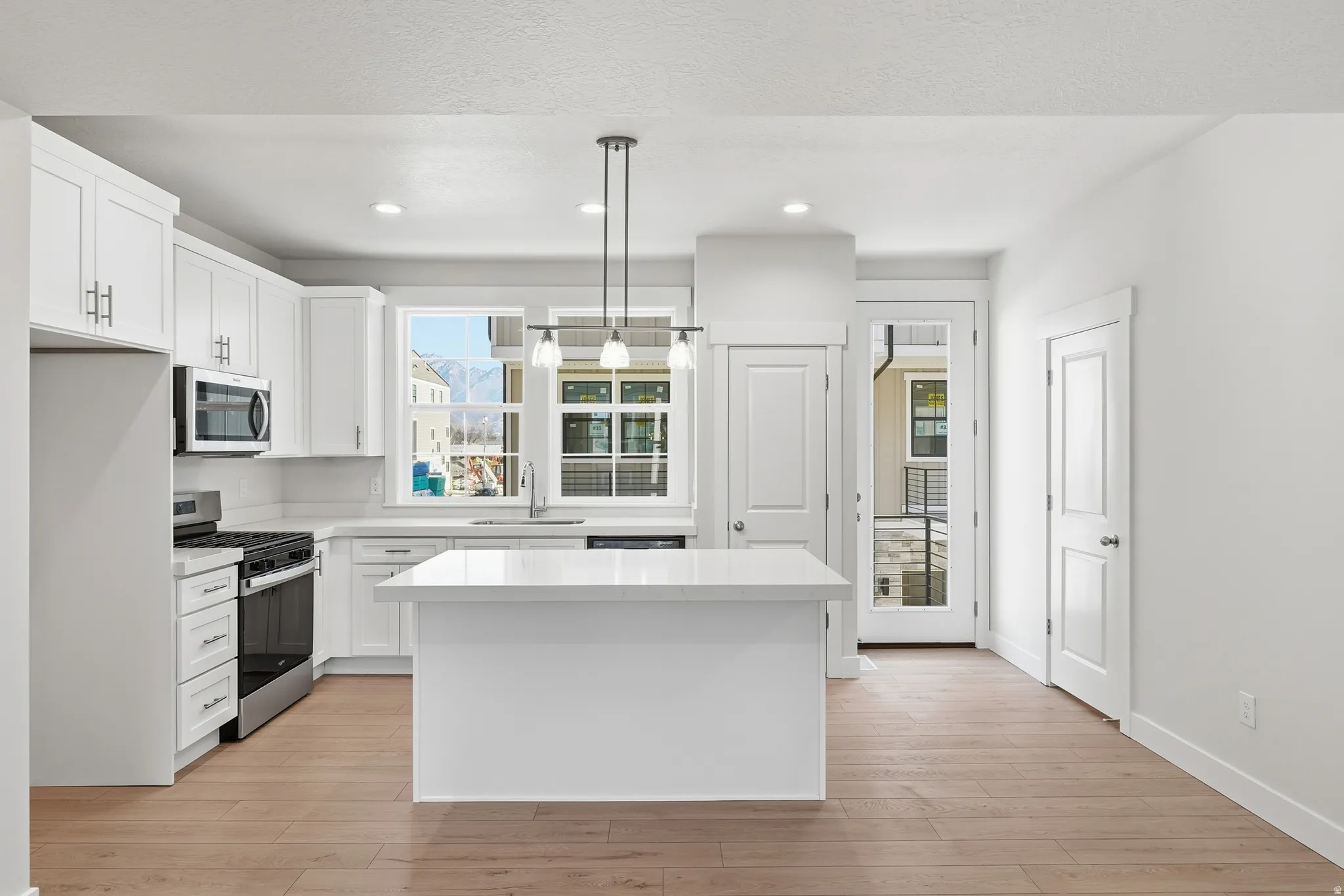 White shaker cabinetry, stainless steel appliances, central island with solid surface countertop, wood-finish flooring, and pendant lighting