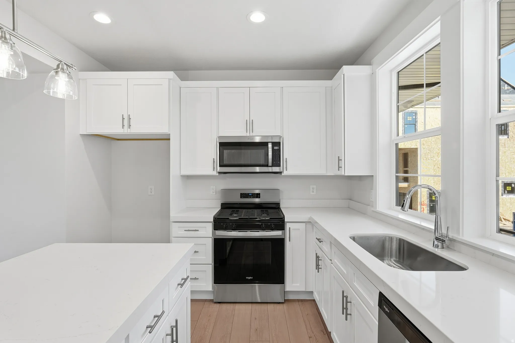 White cabinetry with stainless steel hardware, stainless steel appliances, light-toned wood-finish flooring, and a large window above the sink
