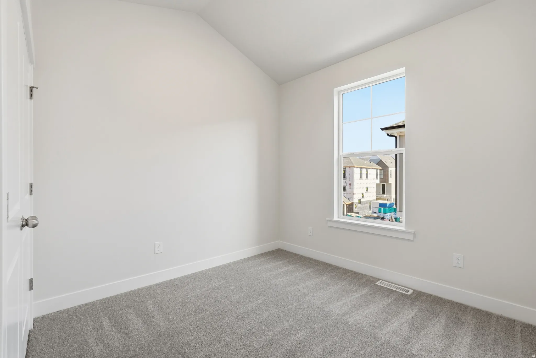 Vaulted ceiling, neutral wall tones, gray carpet, white trim, and a white framed window