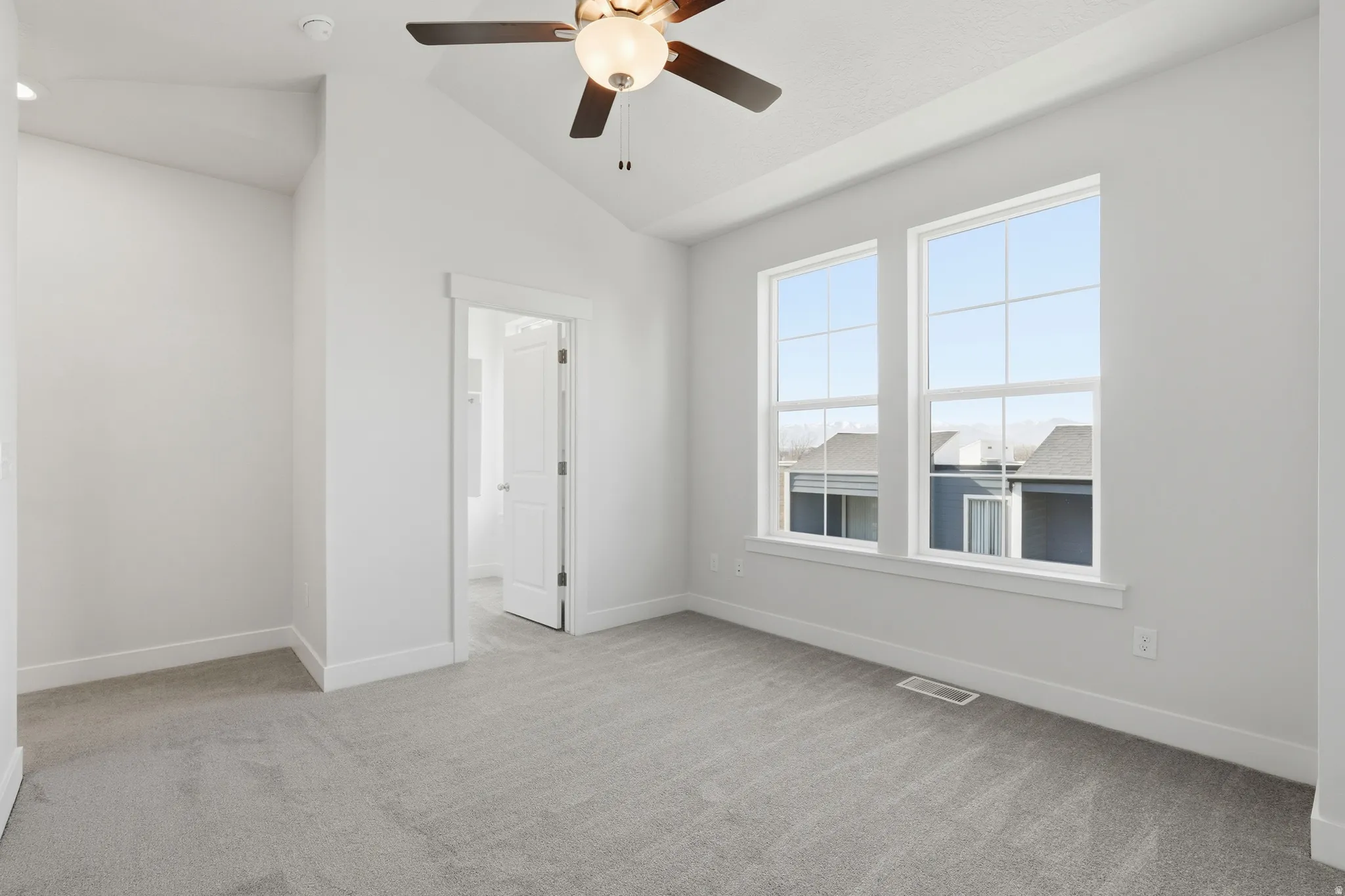 Vaulted ceiling with a ceiling fan, dual windows, and carpet flooring