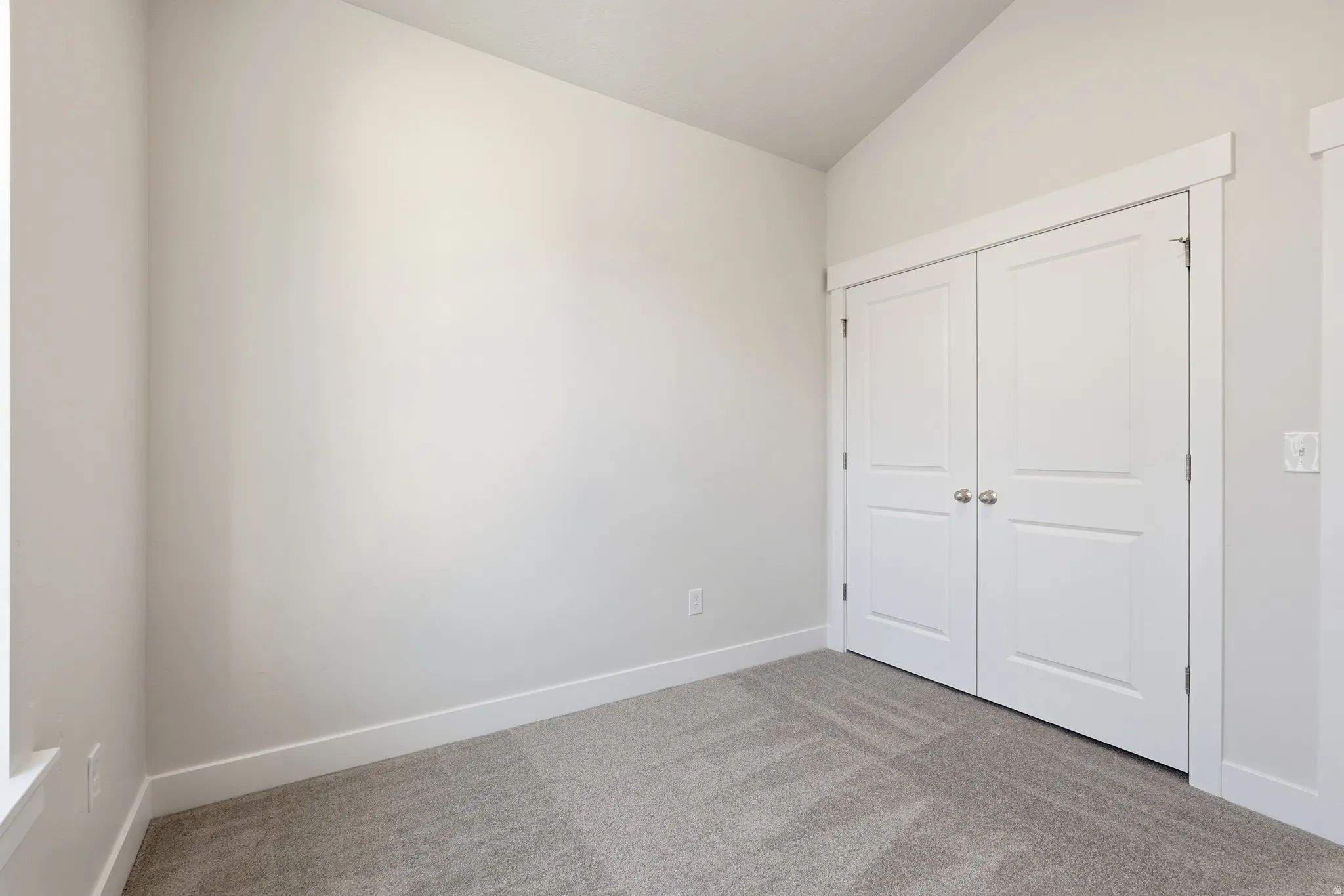 Vaulted ceiling, neutral paint, gray carpeting, white trim, and white bi-fold doors