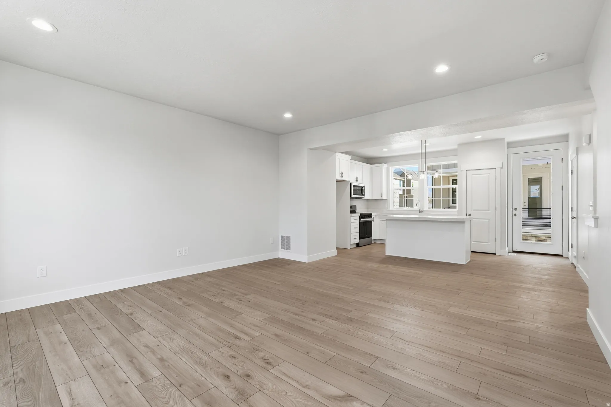 Open-concept living area with wood-finish flooring, recessed lighting, and a white kitchen featuring stainless steel appliances and a breakfast bar