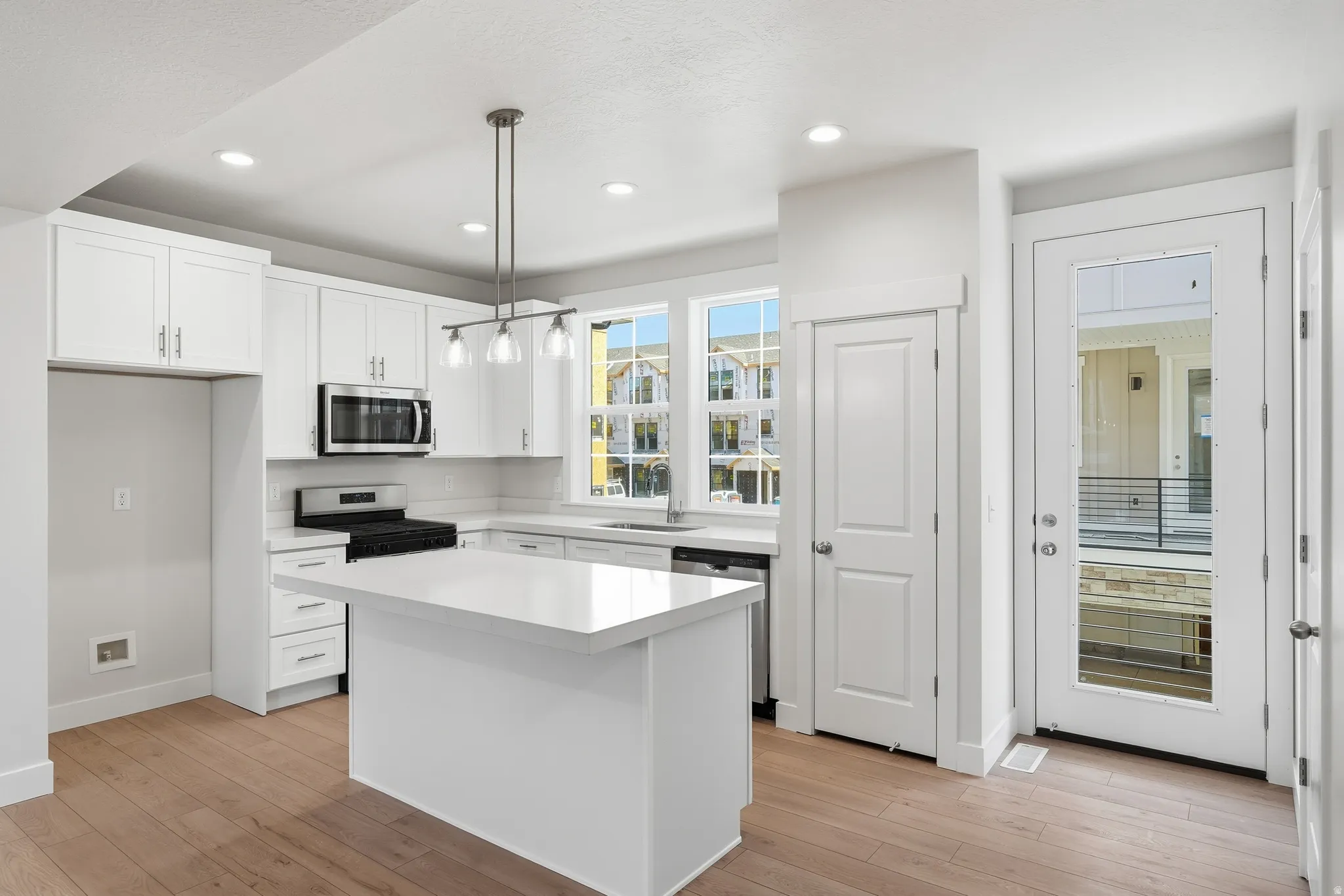 Modern kitchen featuring white shaker cabinetry, stainless steel appliances, a center island with a solid surface countertop, wood-finish flooring, and recessed lighting