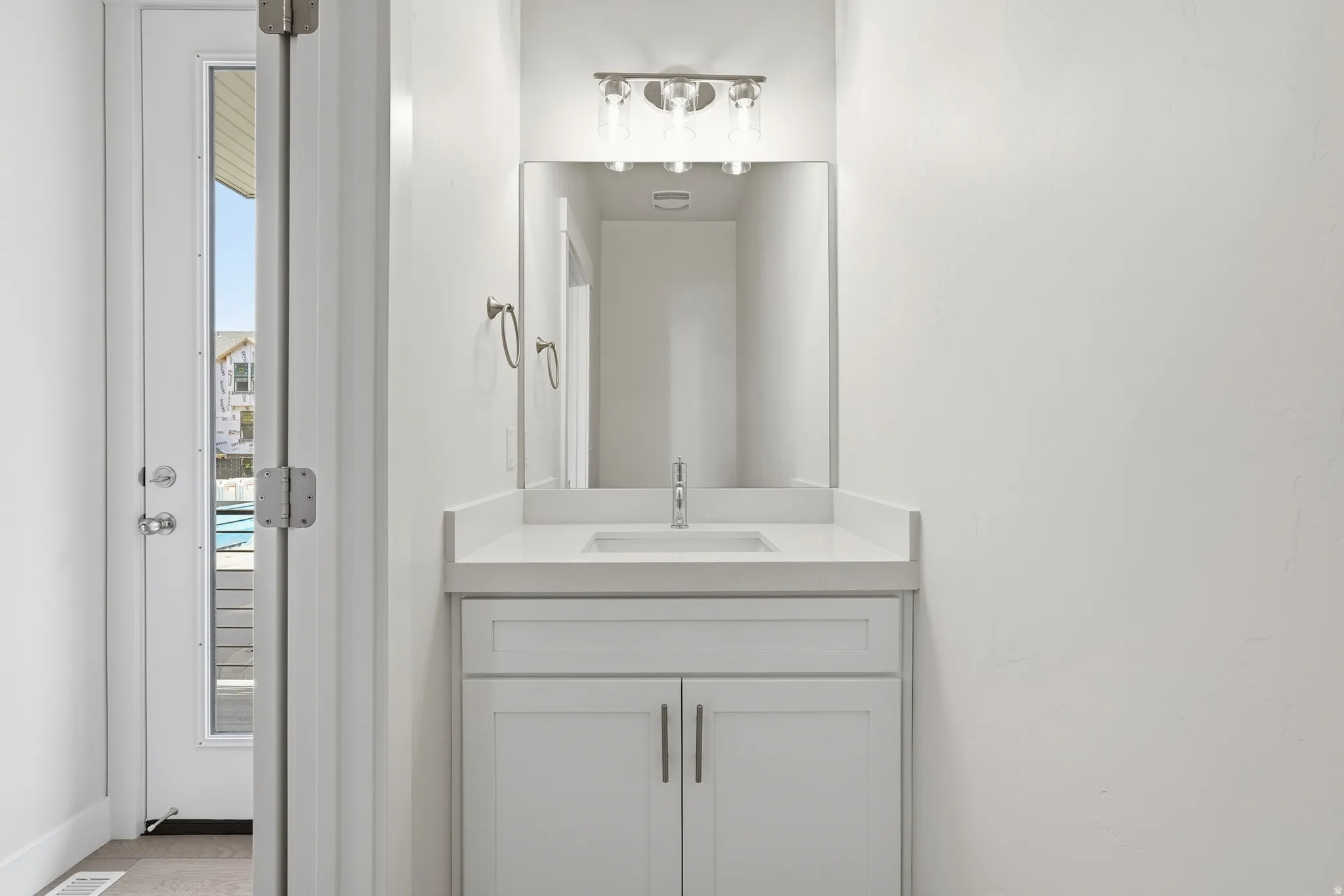 White shaker vanity with a single basin sink, white countertop, and brushed nickel hardware
