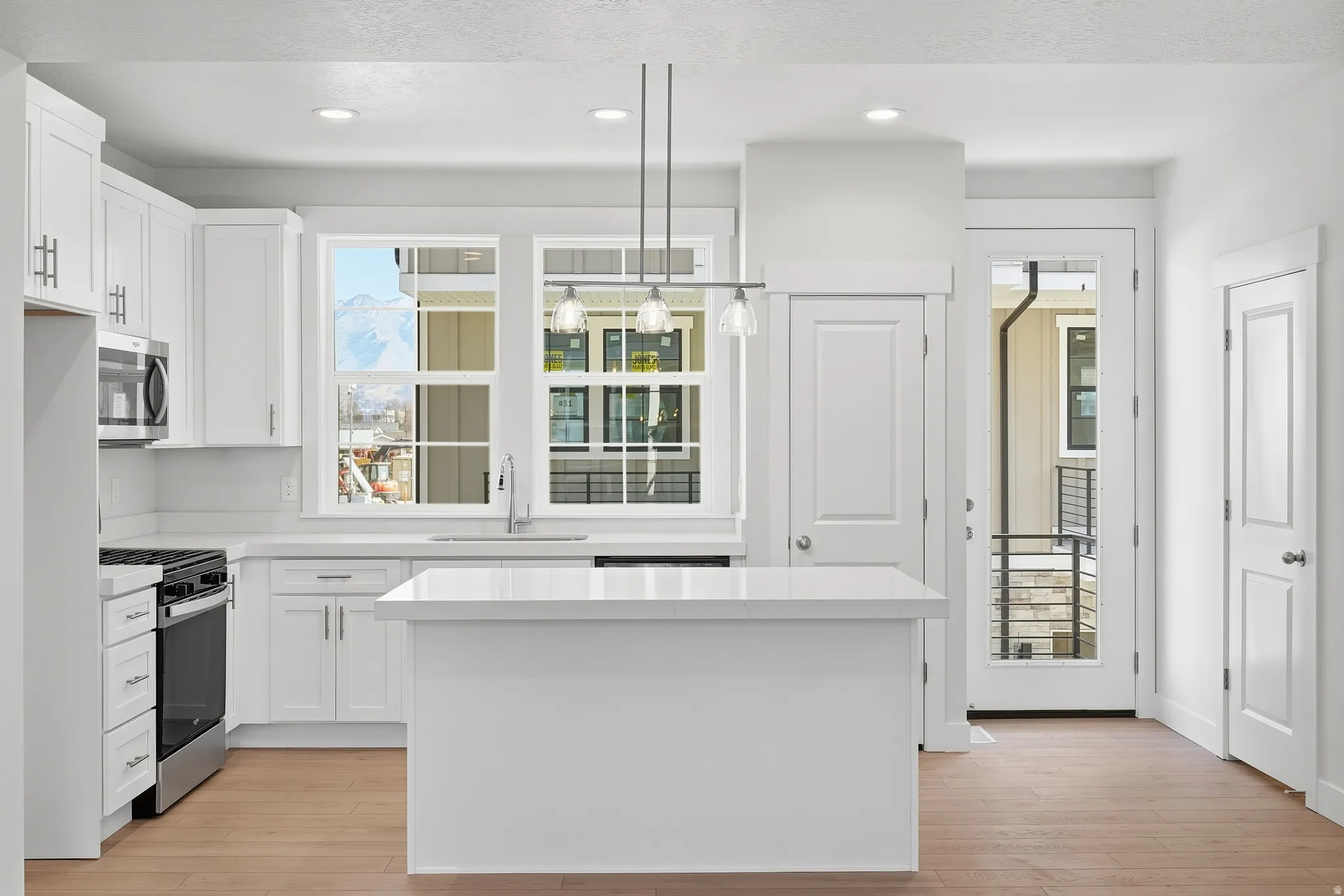 Bright kitchen featuring white cabinetry, a central island, stainless steel appliances, and wood-finish flooring