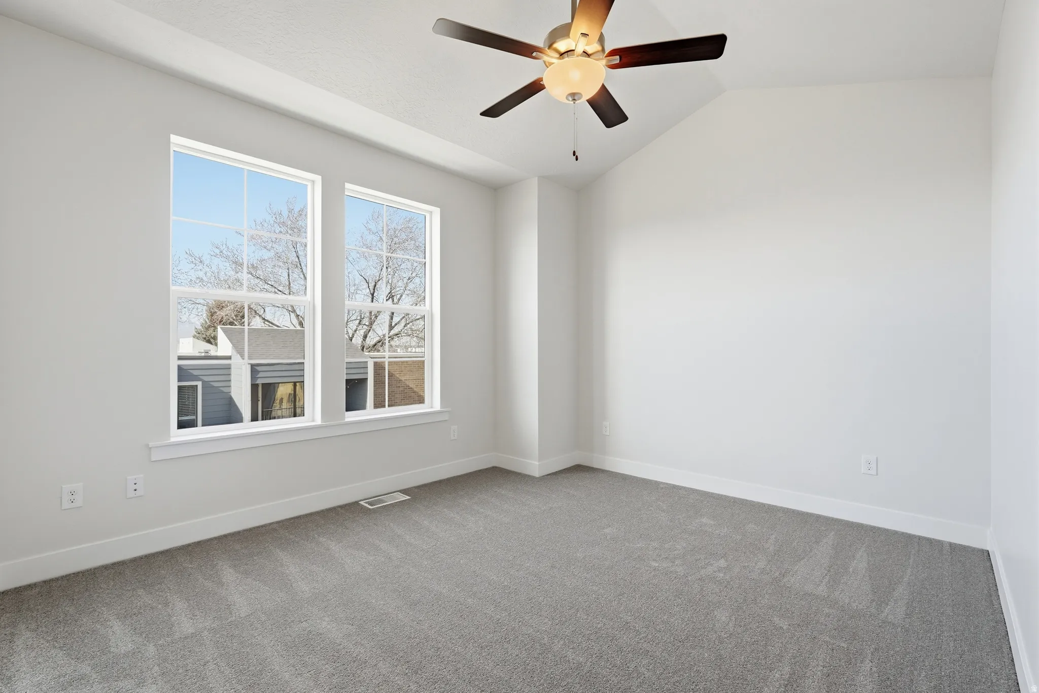Vaulted ceiling, two large windows, ceiling fan with integrated lighting, wall-to-wall carpeting, and white trim