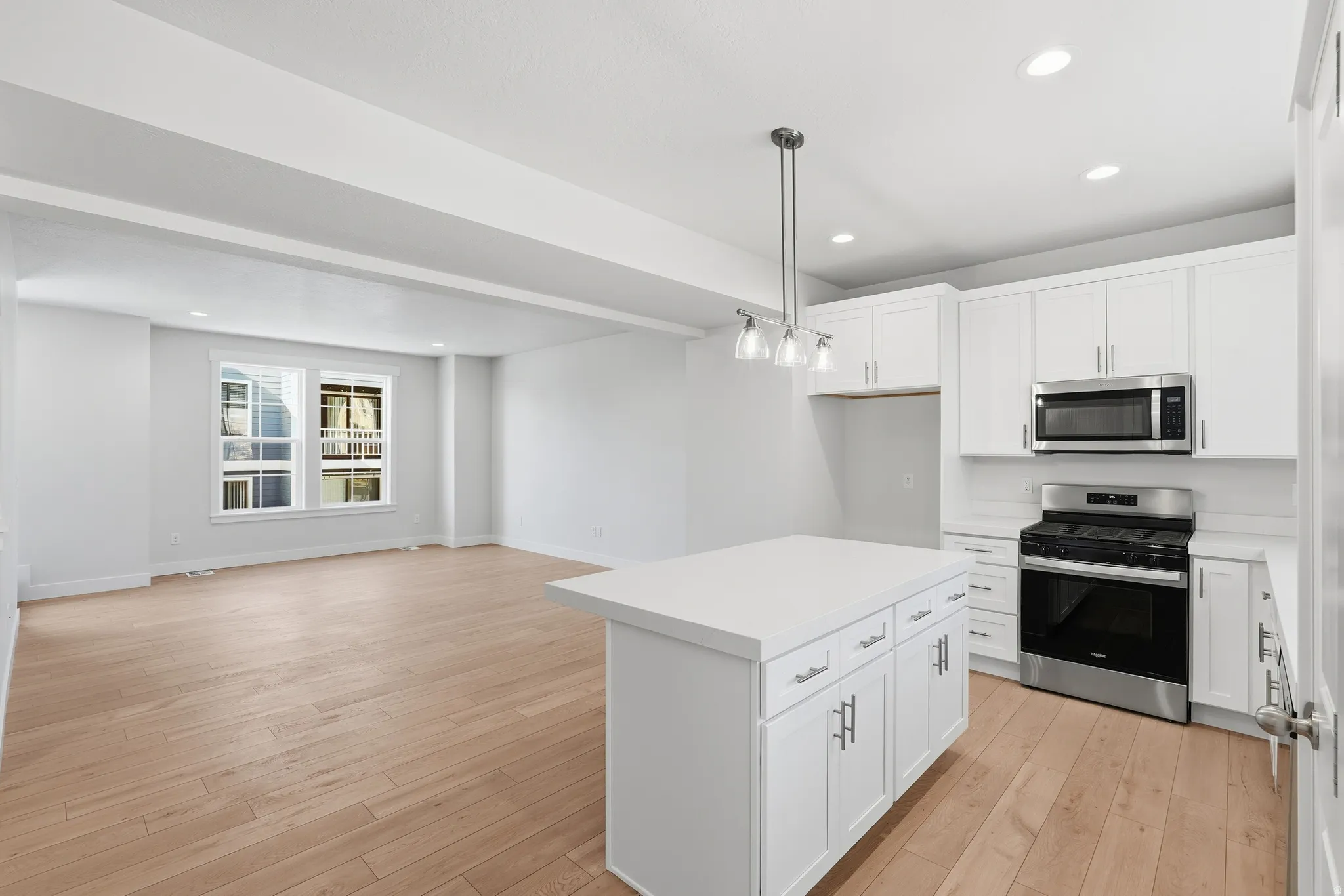 Open-concept kitchen and living area featuring wood-finish flooring, white shaker cabinetry, stainless steel appliances, a kitchen island with storage, and recessed lighting