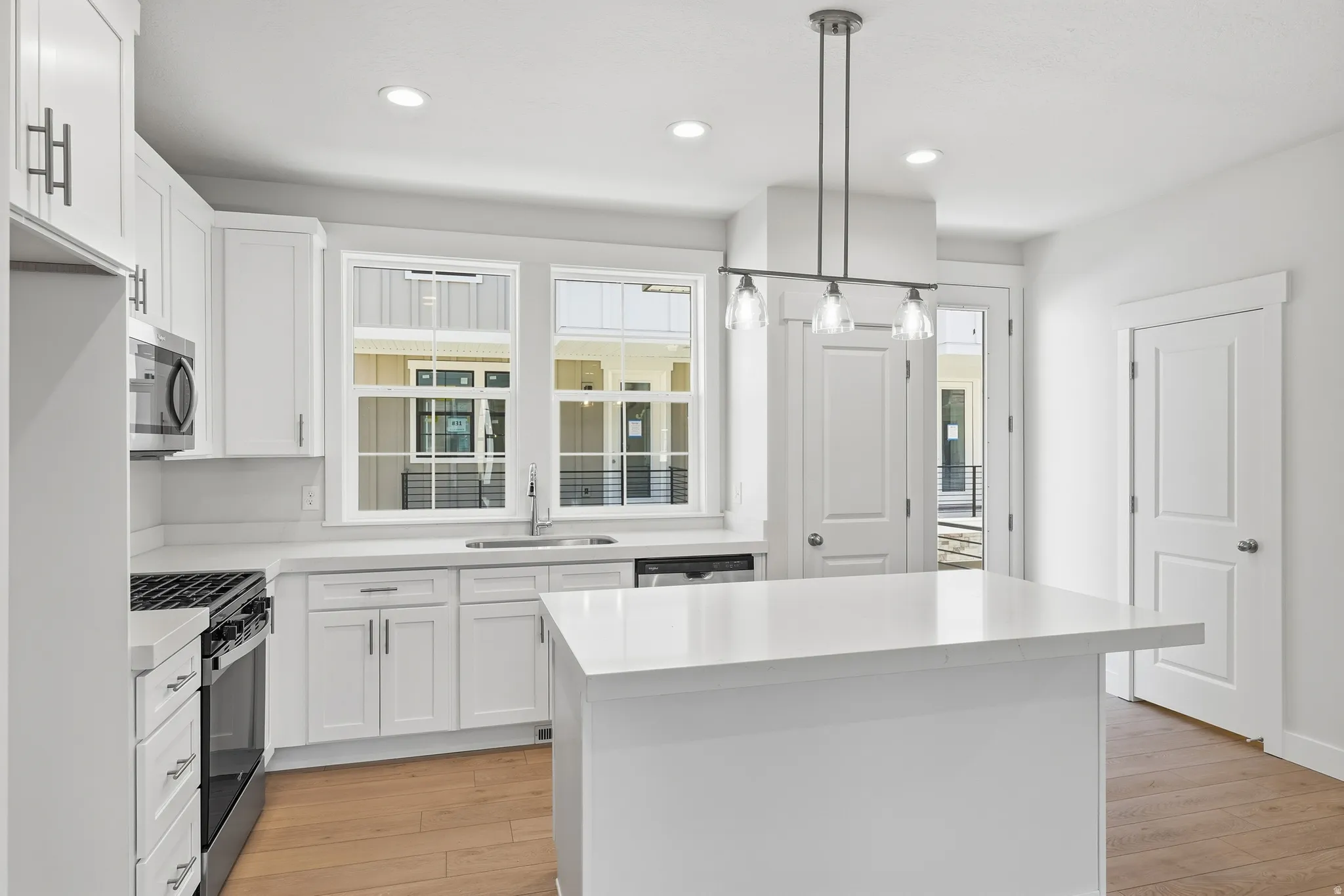 White cabinetry with brushed nickel hardware, stainless steel appliances, a center island with a solid surface countertop, wood-finish flooring, and recessed lighting