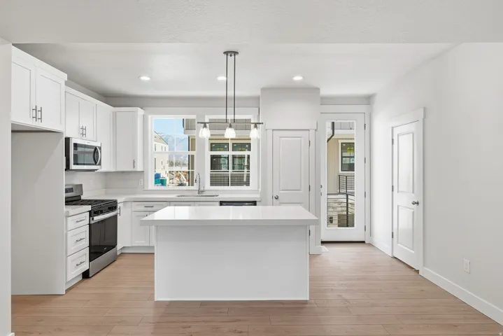 White shaker cabinetry, stainless steel appliances, central island with solid surface countertop, wood-finish flooring, and pendant lighting