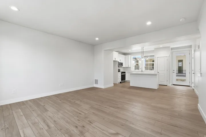 Open-concept living area with wood-finish flooring, recessed lighting, and a white kitchen featuring stainless steel appliances and a breakfast bar