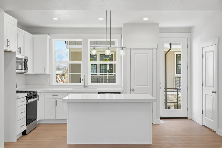 Bright kitchen featuring white cabinetry, a central island, stainless steel appliances, and wood-finish flooring