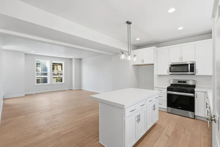 Open-concept kitchen and living area featuring wood-finish flooring, white shaker cabinetry, stainless steel appliances, a kitchen island with storage, and recessed lighting