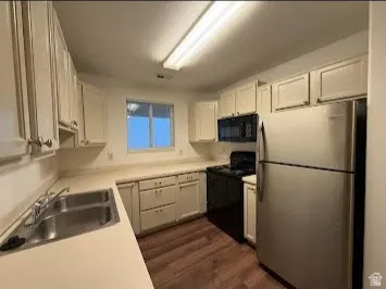 Kitchen featuring extensive cabinetry, laminate countertops, wood-finish flooring, a stainless steel refrigerator, and a window