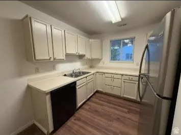 L-shaped kitchen with white cabinetry, light-toned countertops, wood-finish flooring, and a stainless steel refrigerator