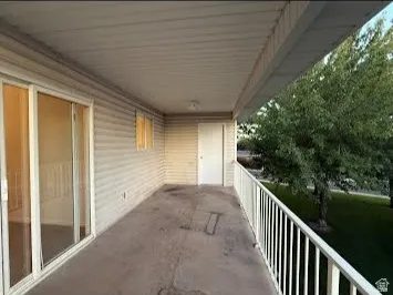 Covered balcony featuring white vinyl siding, sliding glass door, overhead lighting, and white metal railing