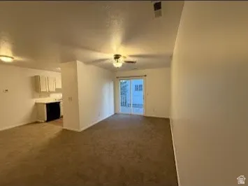 Expansive open-concept living area featuring neutral carpeting, a ceiling fan, and sliding glass doors
