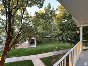 Balcony with white metal railing overlooking a landscaped green space with mature trees and a concrete pathway