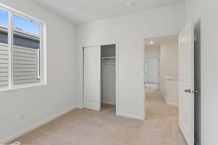 White walls with carpeted flooring, featuring a window and a closet with sliding doors