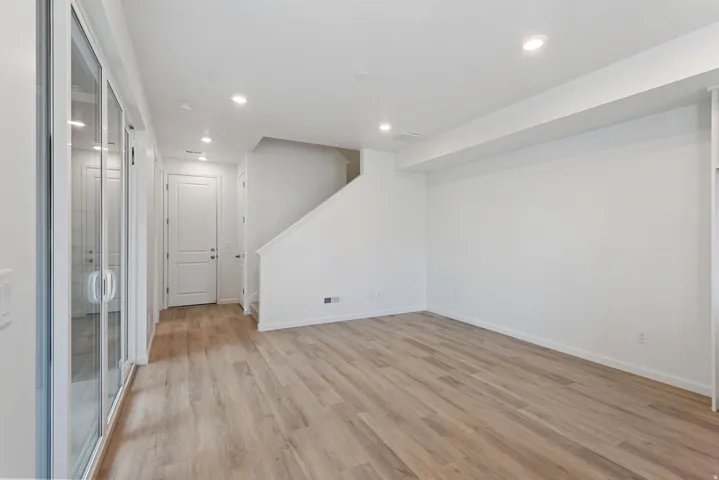 Recessed lighting, wood-finish flooring, white walls, white trim, and a white interior door